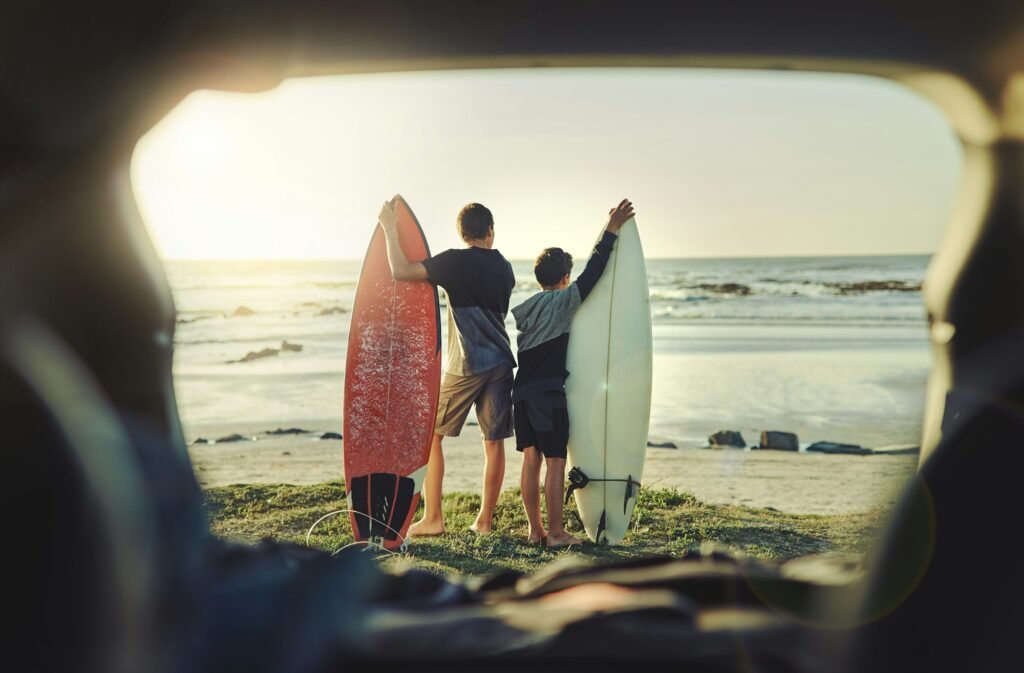 Rearview shot of two brothers holding their surfboards while standing on the beach